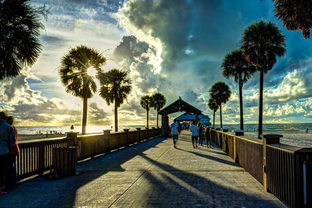 Photo of boardwalk in a beach in Florida with trees on both sides and people walking in the pathway.