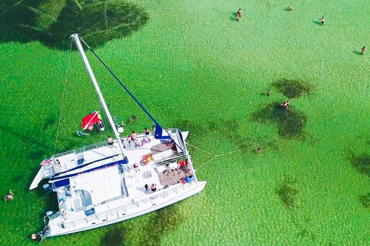 Aerial view of a big white catamaran cruise with guests having a fun boat time in the middle of crystal clear green waters in Shell Island Florida