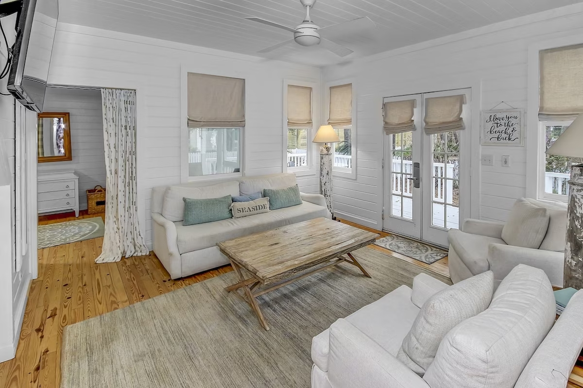 Sea Shack Seaside Cottage living area with wooden floors and a wooden center table with 2 couches facing and a clean white room interior