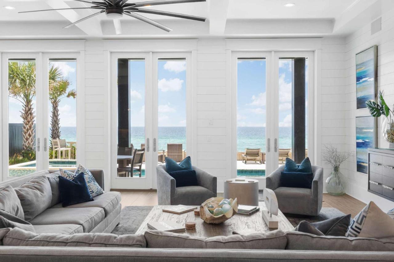 Seaside Serenity #54 rental cozy living room with gray couches and high ceiling glass windows overlooking an outdoor pool and a beautiful beach view of Santa Rosa Beach