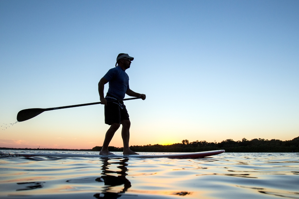 man paddle boarding in the Florida waters with a sunset background