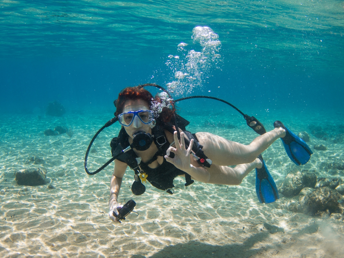 a woman making an okay sign underwater while scuba diving in the clear waters of Cozumel Bahamas