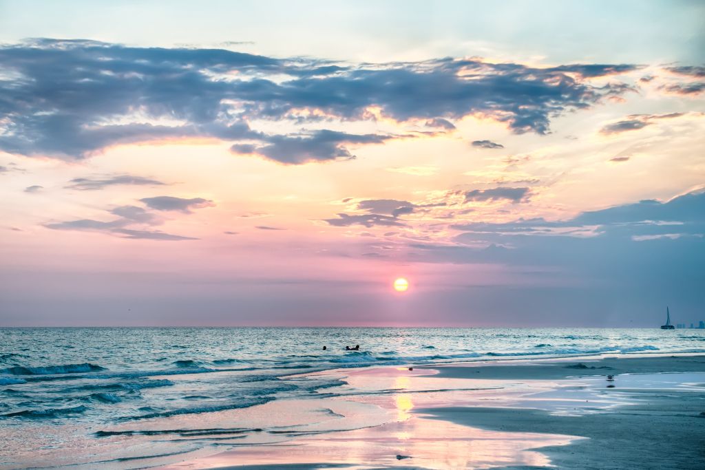 Peaceful Florida beach at sunset with pastel-colored sky, gentle waves, and a sailboat on the horizon—capturing the allure of a tranquil vacation getaway.