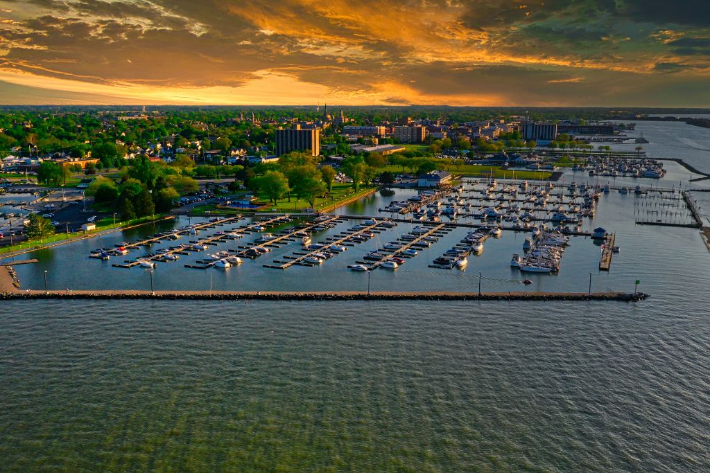Aerial view of Sandusky, Ohio, featuring a large marina filled with boats along the Lake Erie waterfront and the city skyline beneath a dramatic golden sunset.