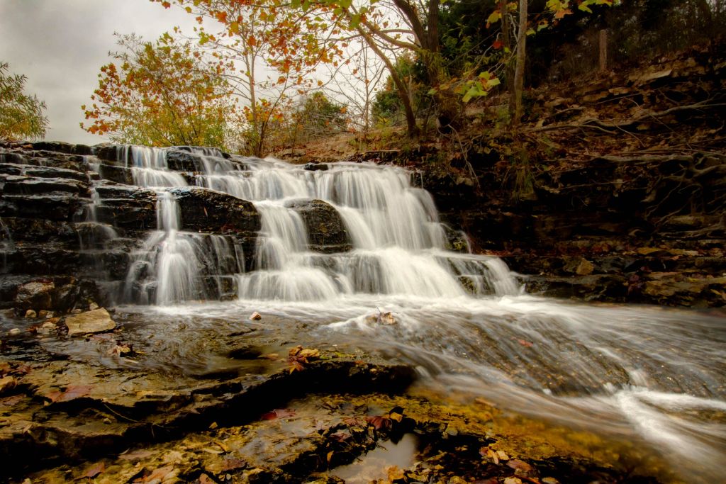 Scenic waterfall cascading over layered rocks surrounded by autumn foliage in Bella Vista, Arkansas.